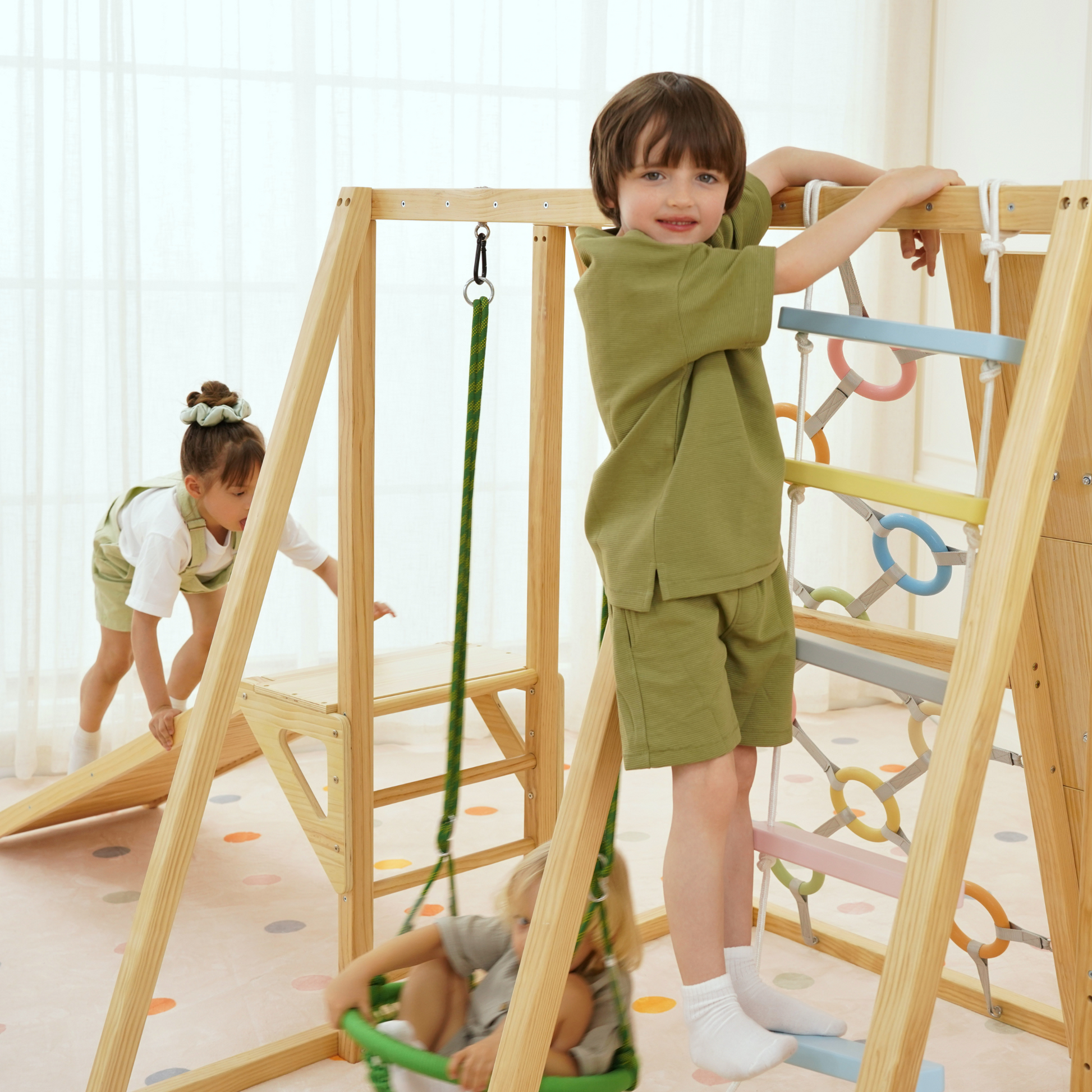 Child climbing colorful rope ladder while another swings and third explores slide ramp on Sweetgum climber