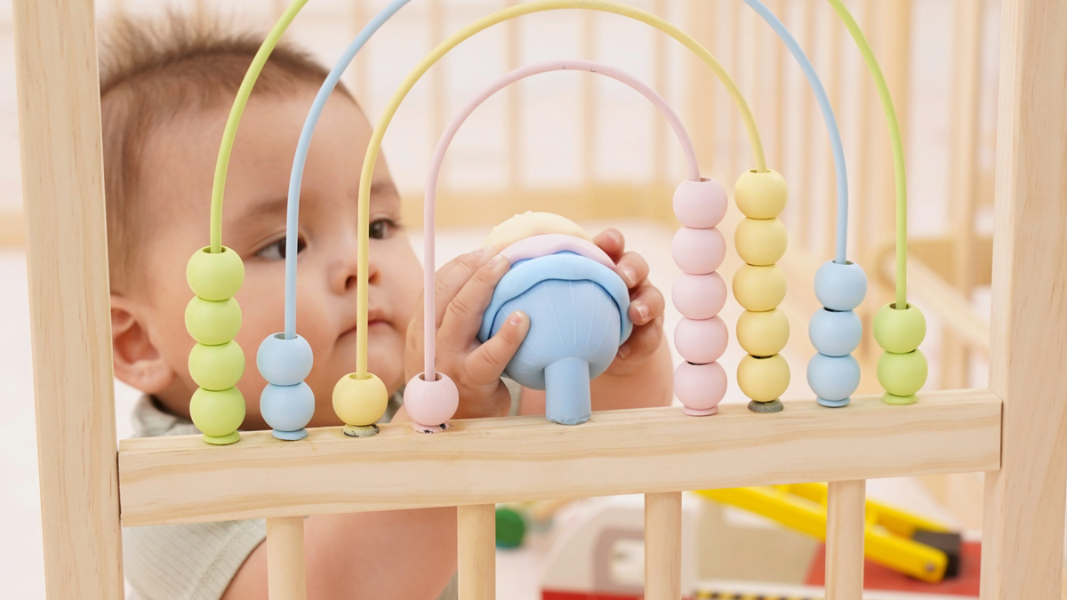 Close-up of the Montessori activity panel with geometric blocks and tactile ribbons on the Avenlur wooden playpen