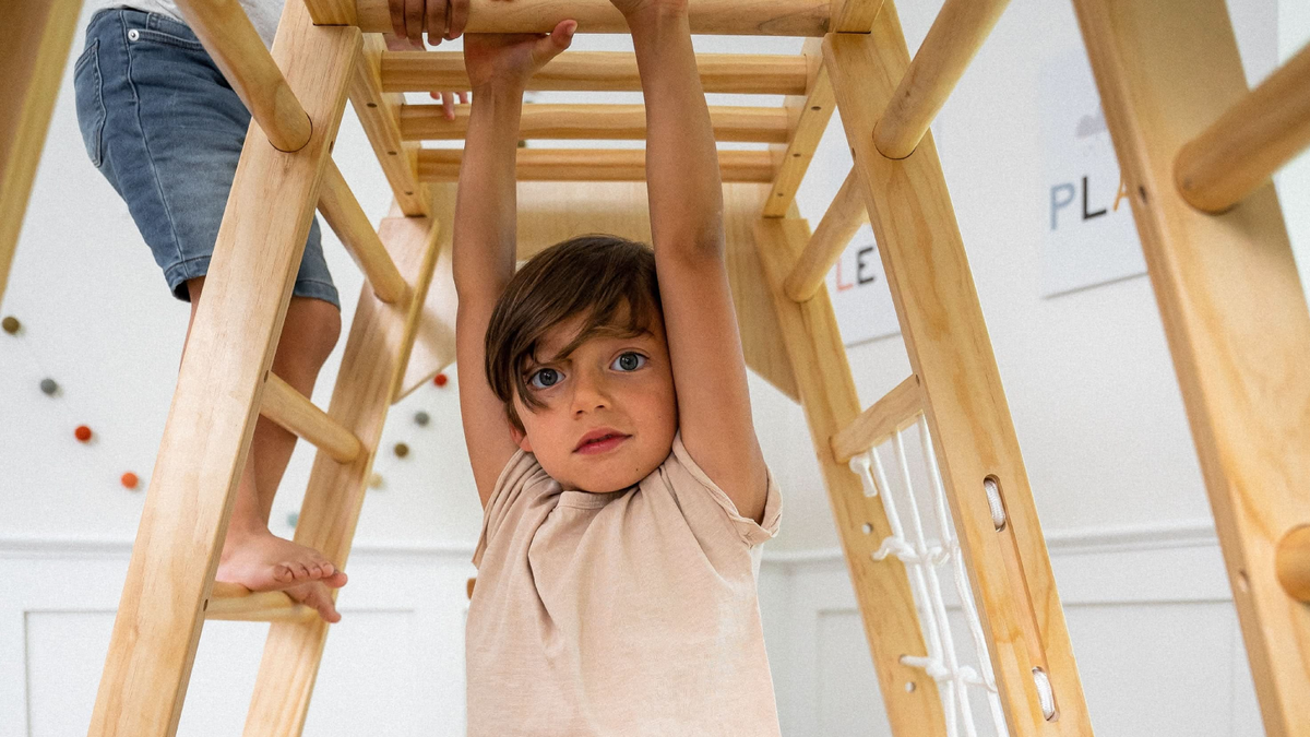 Avenlur Magnolia indoor wooden jungle gym with climbing wall, slide and monkey bars in a bright playroom