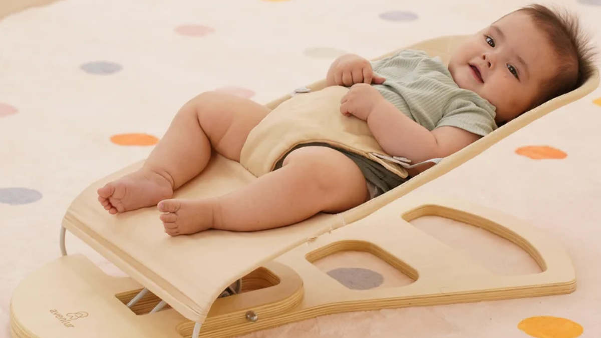 Baby resting in the Avenlur Fir wooden baby bouncer with play arch