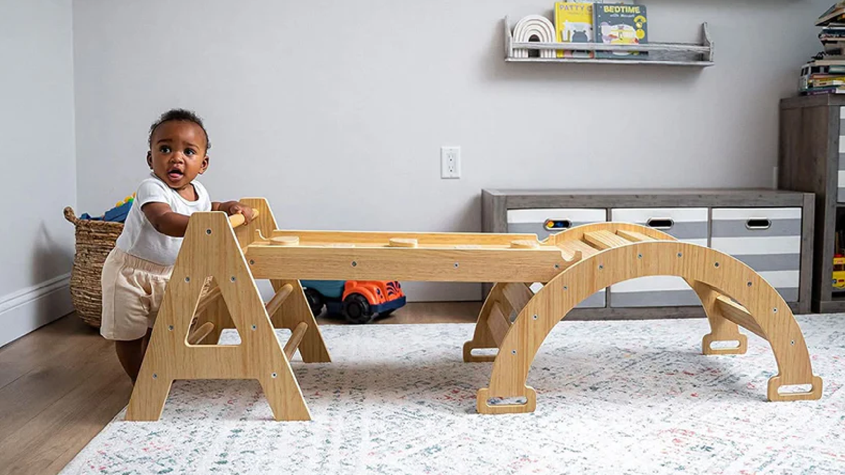 Toddler climbing an Avenlur Hazel Pikler triangle set with slide and rocker in a bright playroom