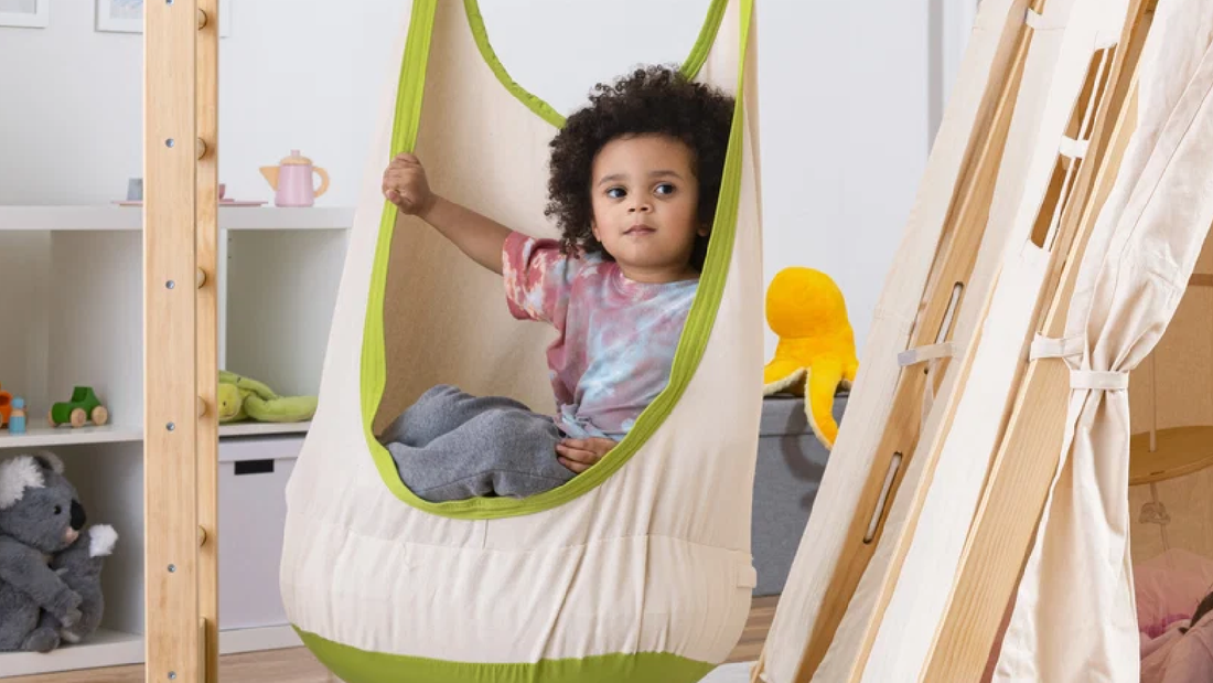 Child relaxing in an Avenlur cocoon sensory swing hanging from a wooden climber
