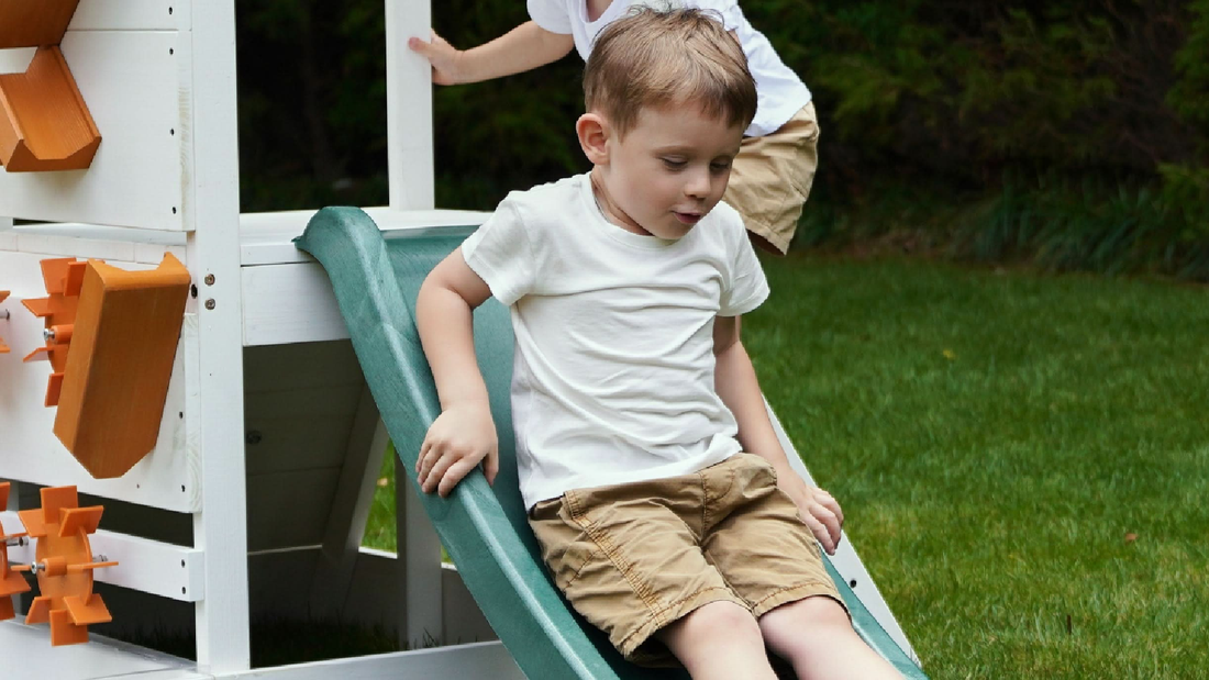 Kids sliding down the Avenlur Aloe wooden outdoor playhouse slide in a backyard