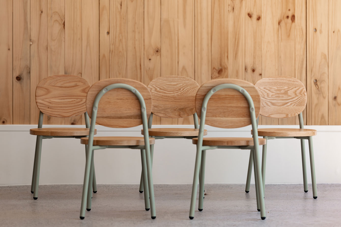 Set of wooden chairs with metal frames against a wooden paneled wall.
