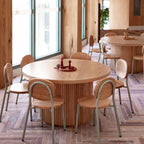 Wooden dining tables and chairs in a modern indoor setting with large windows.