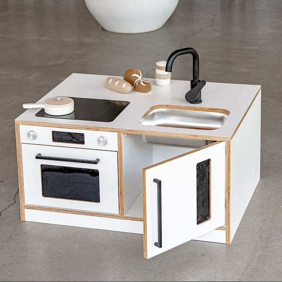 Children's play kitchen set with white surface, black stove, oven, and sink on a gray floor.