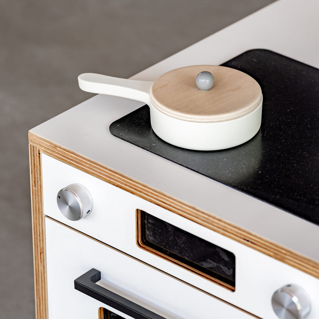 White stove with black cooktop and wooden accents, featuring a small white pot with a wooden lid.