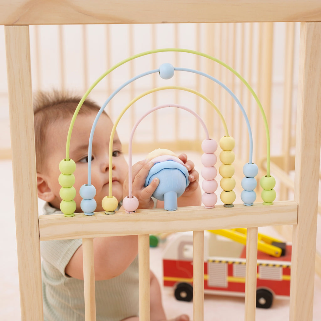 Close-up of the Montessori activity panel with geometric blocks and tactile ribbons on the Avenlur wooden playpen