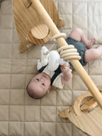 Baby on a play mat during tummy time beside the Avenlur Rocket gym
