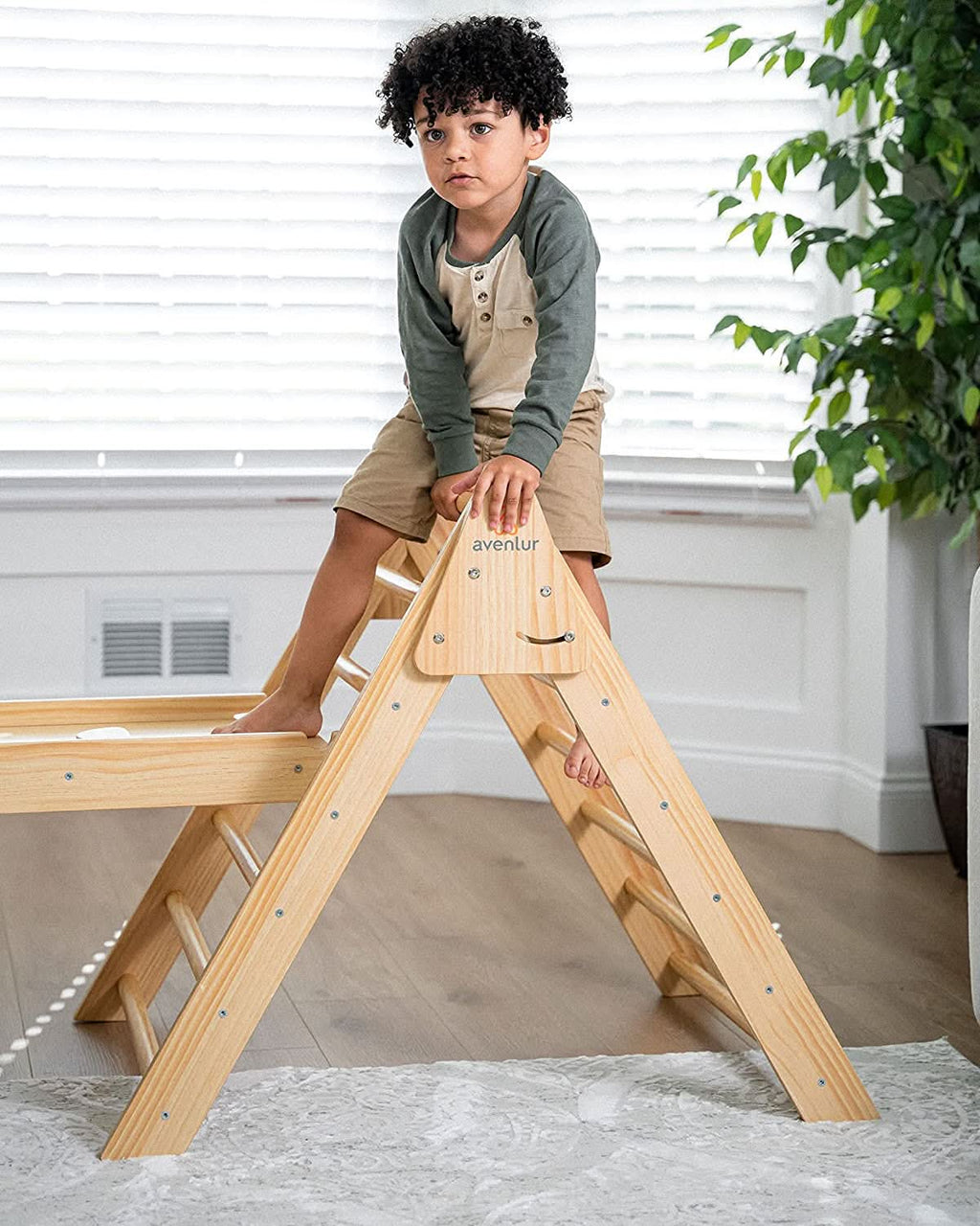Child sitting on top of Avenlur Hazel Pikler Triangle in bright playroom