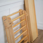 Close-up of folded Avenlur Hazel Pikler Triangle and slide stored upright against wall